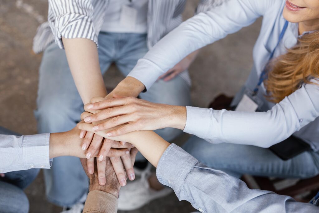 Grupo de pessoas colocando as mãos umas sobre as outras em gesto de união e trabalho em equipe.