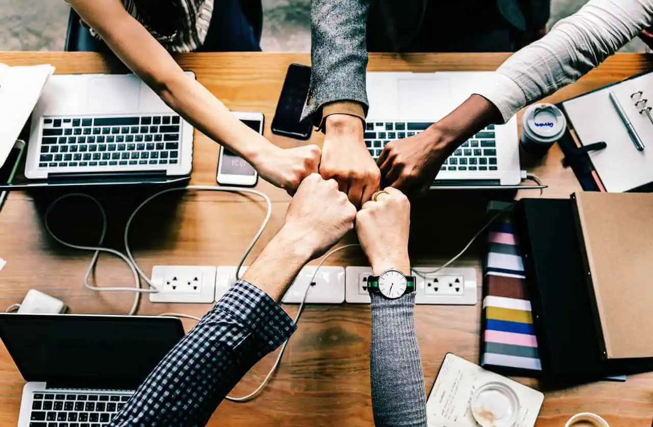 Pessoas unindo as mãos sobre uma mesa de trabalho, simbolizando trabalho em equipe